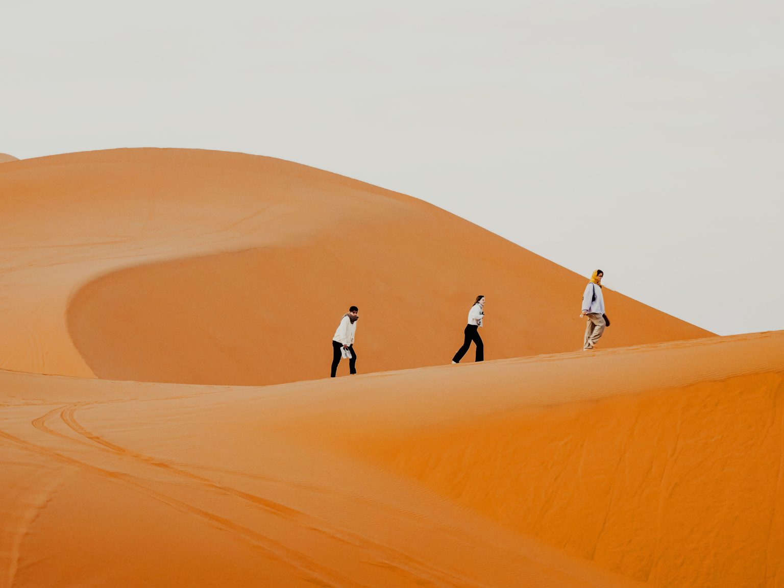 Three women walking together across a Sahara dune in Morocco